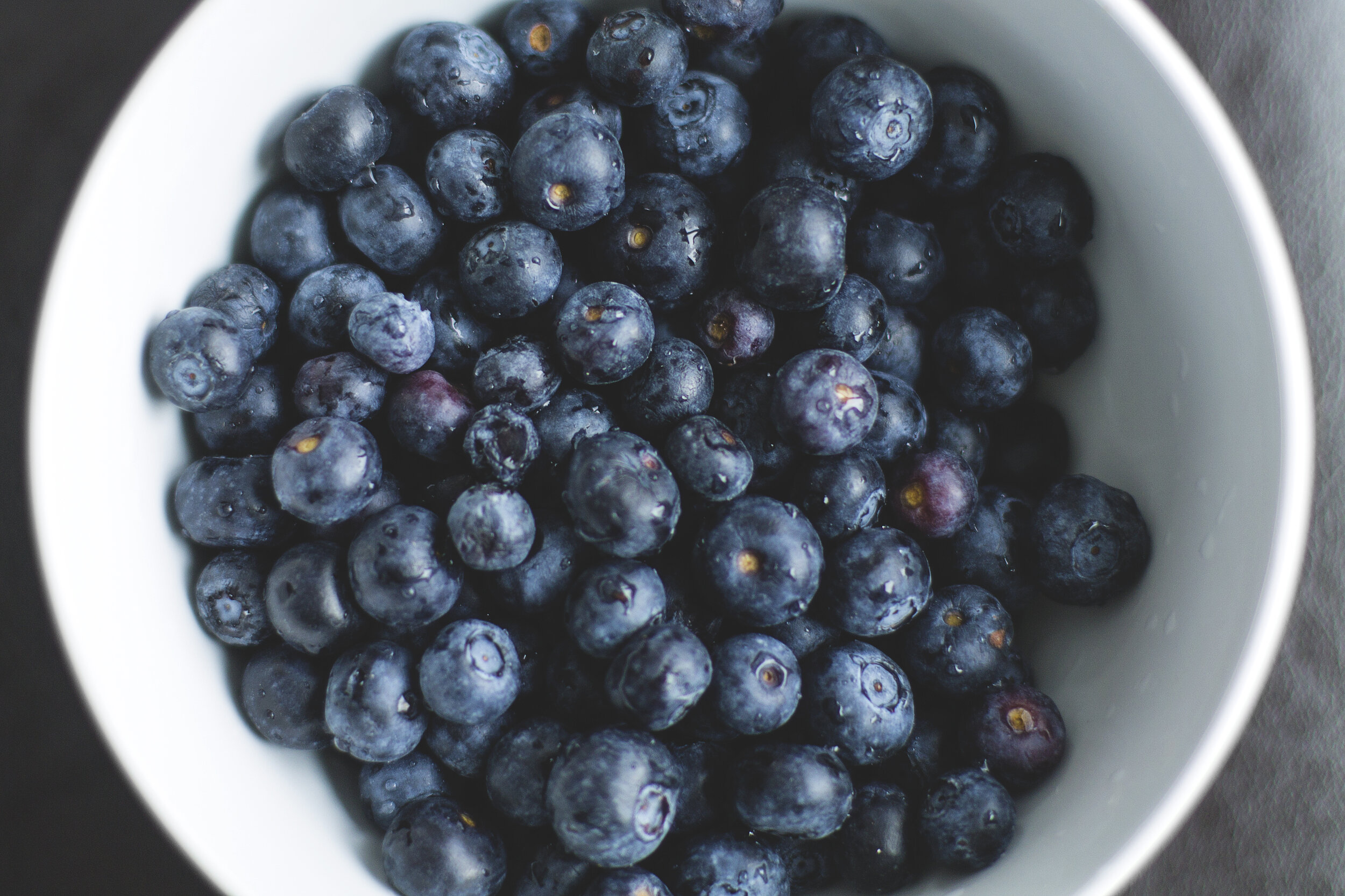 A bowl filled with fresh, plump blueberries, showcasing their vibrant blue color and a few droplets of water, highlighting their freshness and appeal as a healthy snack.